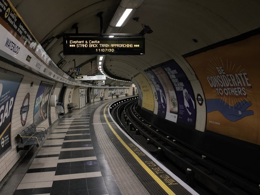 An empty section of the Waterloo underground station platform featuring a curved train track bordered by yellow safety lines and tactile paving. The platform surface is covered with black and white ch