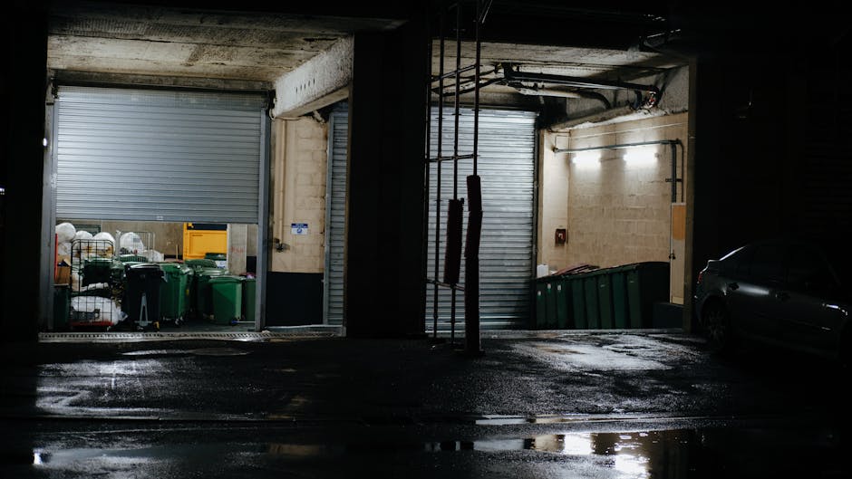 A parking garage interior featuring a white rectangular sign hanging from the ceiling with black text that reads 'NO ENTRY' and flanked by red circular symbols with a white horizontal bar indicating n
